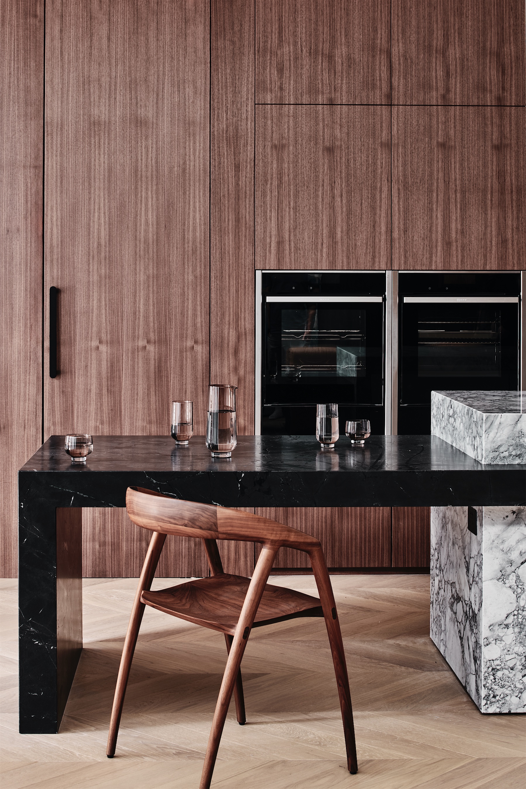 kitchen with walnut joinery, twin wall ovens, a black stone bench, a veined marble island and a timber chair, opus 73, middle park