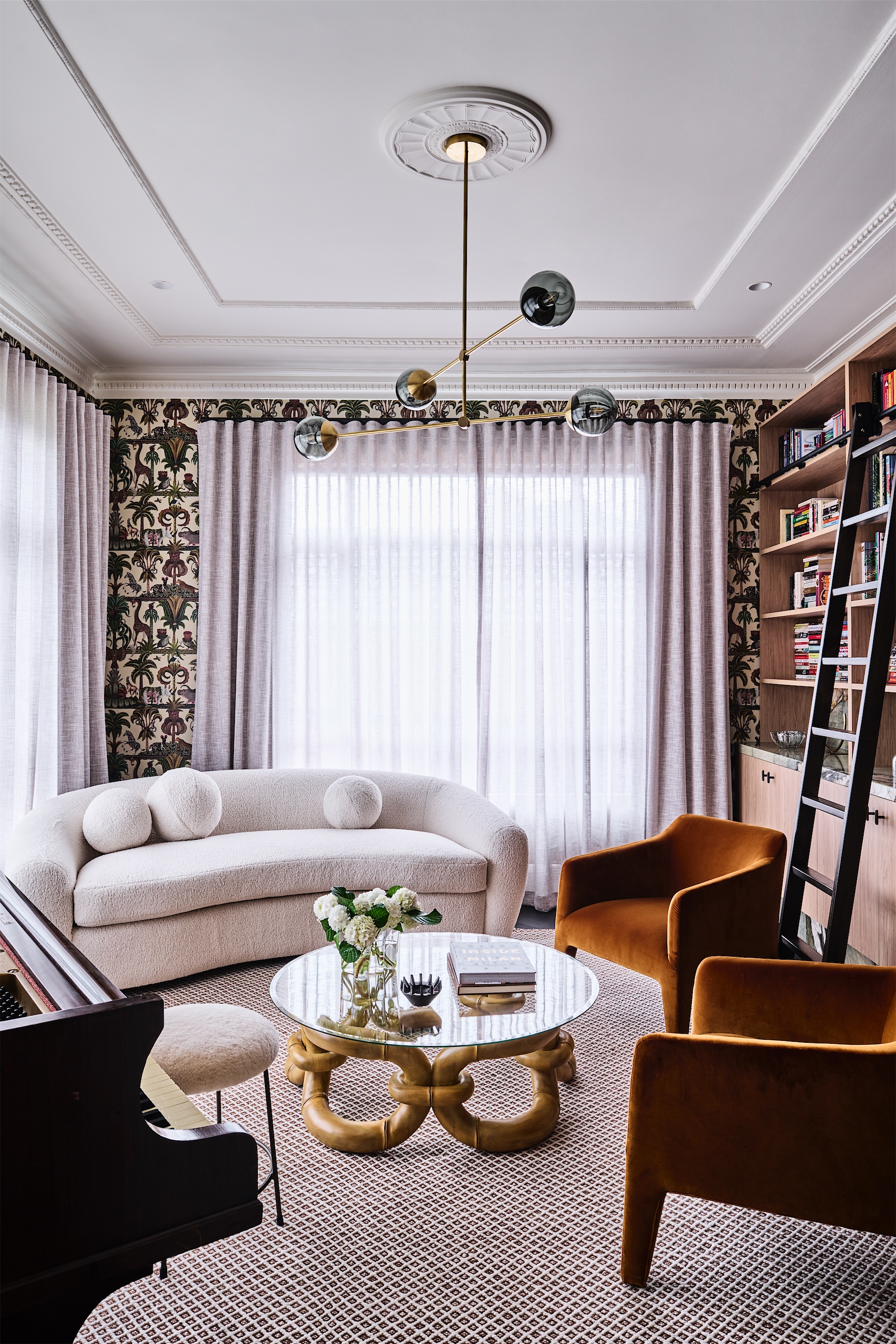 front room with a ceiling rose, curved white sofa, rust velvet armchairs, a gold-based coffee table and a library wall with a ladder, opus 5, caulfield north