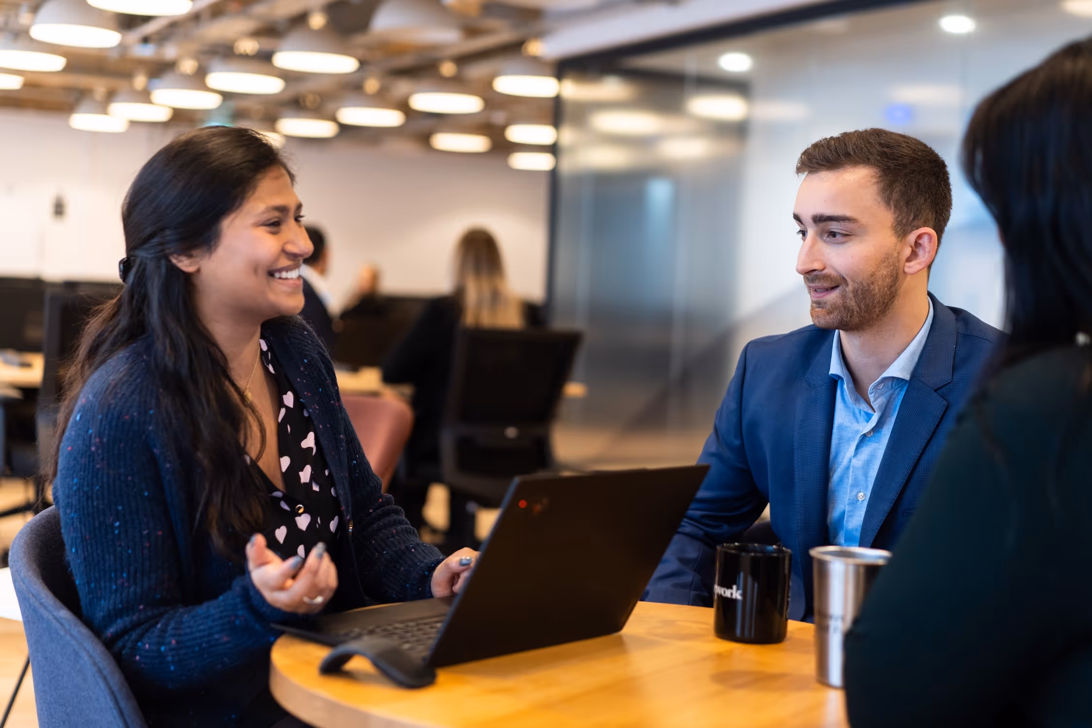 Three business professionals smiling and engaged in discussion around a table in a meeting room.