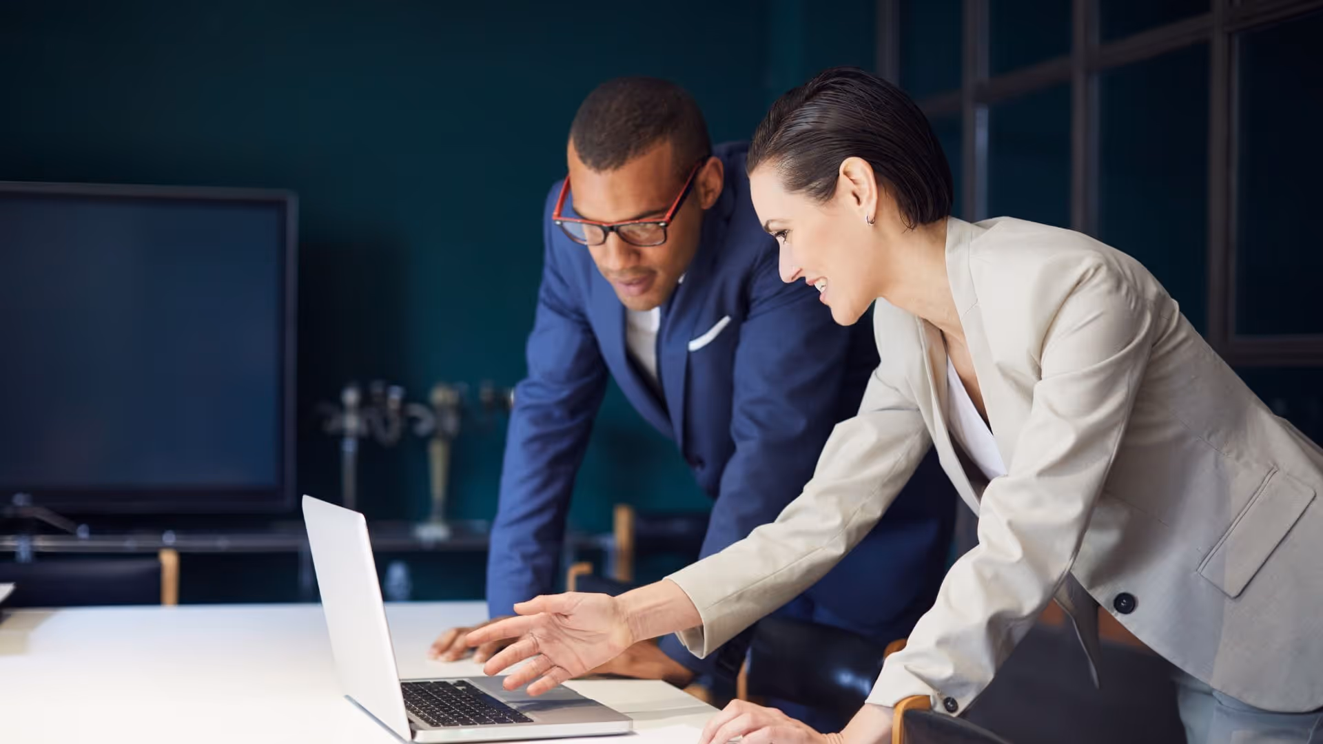 Two business professionals, a man and a woman, reviewing content on a laptop in an office.