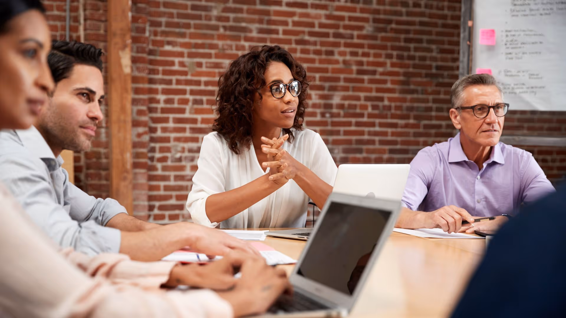 Diverse business team in a meeting room with laptops, listening attentively and discussing.