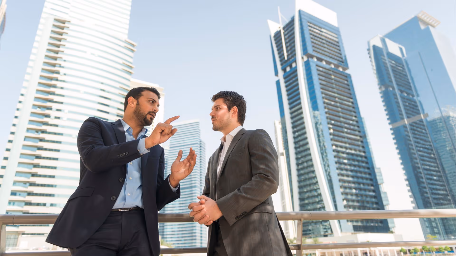 Two businessmen in suits engaged in conversation with modern skyscrapers in the background.