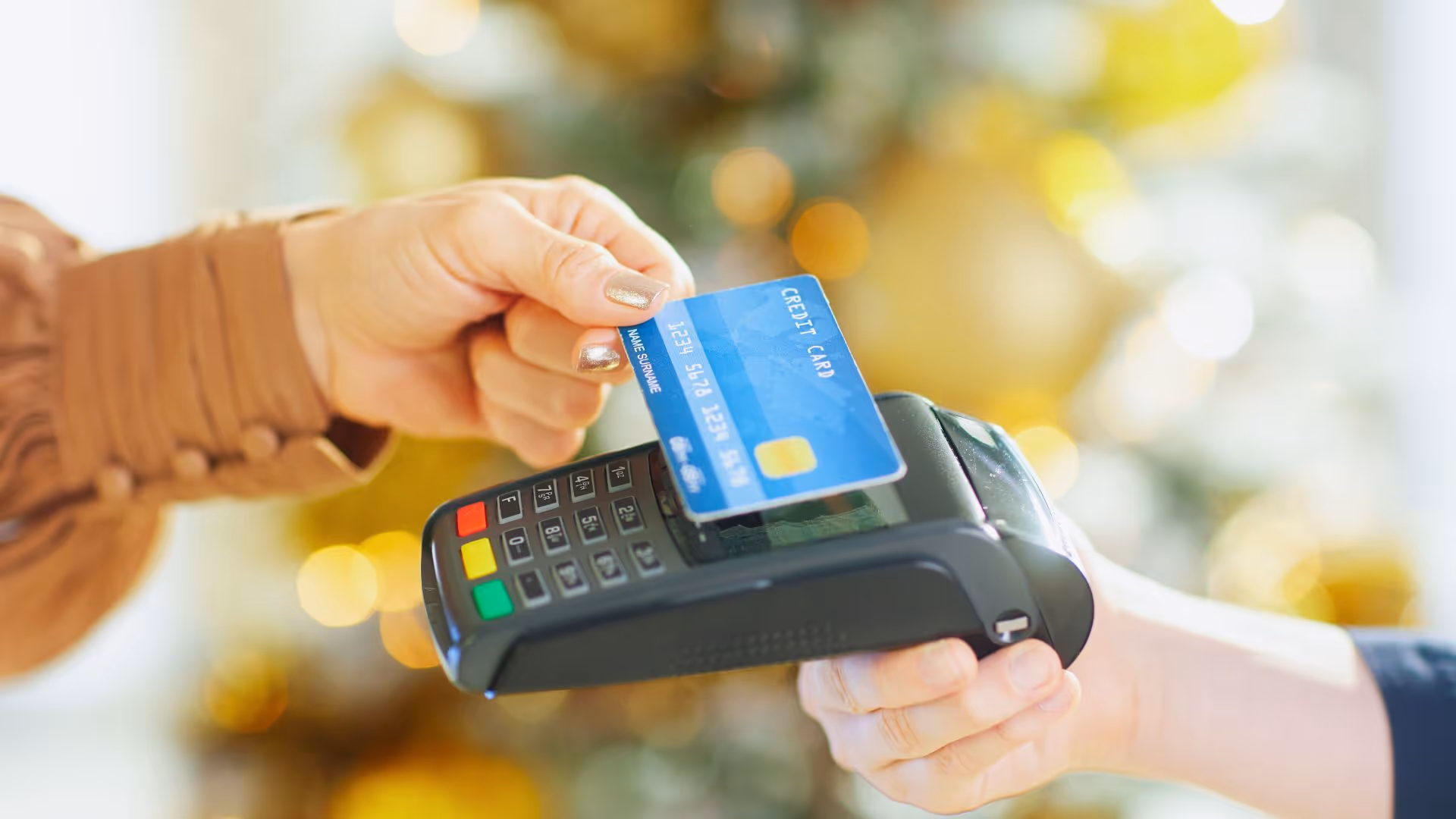 Hand holding a blue credit card near a payment terminal for a contactless transaction.