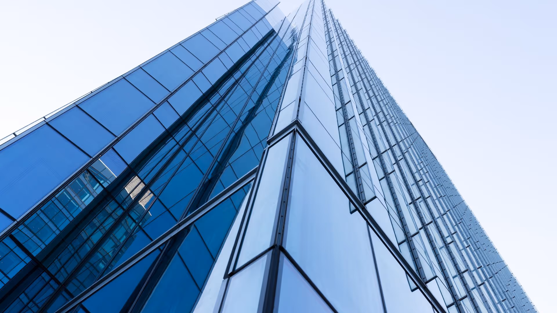 Upward view of a modern skyscraper with glass and steel facade reflecting the sky.