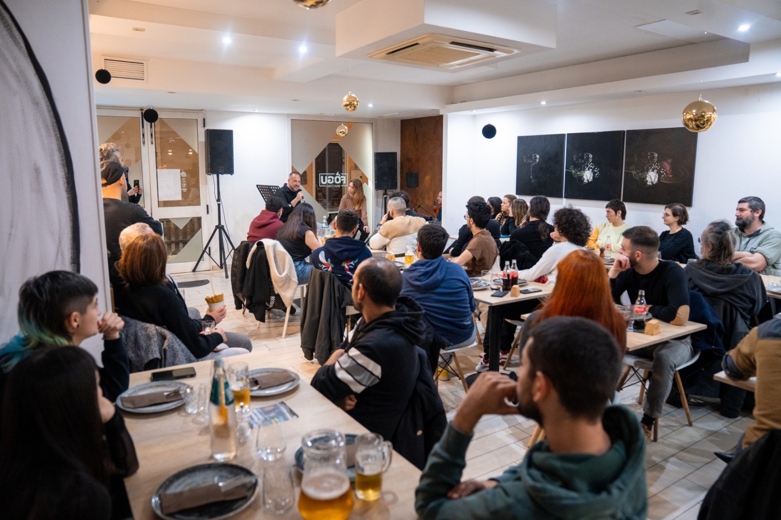 Un gruppo di persone sedute ascolta una presentazione o discussione in una sala luminosa.