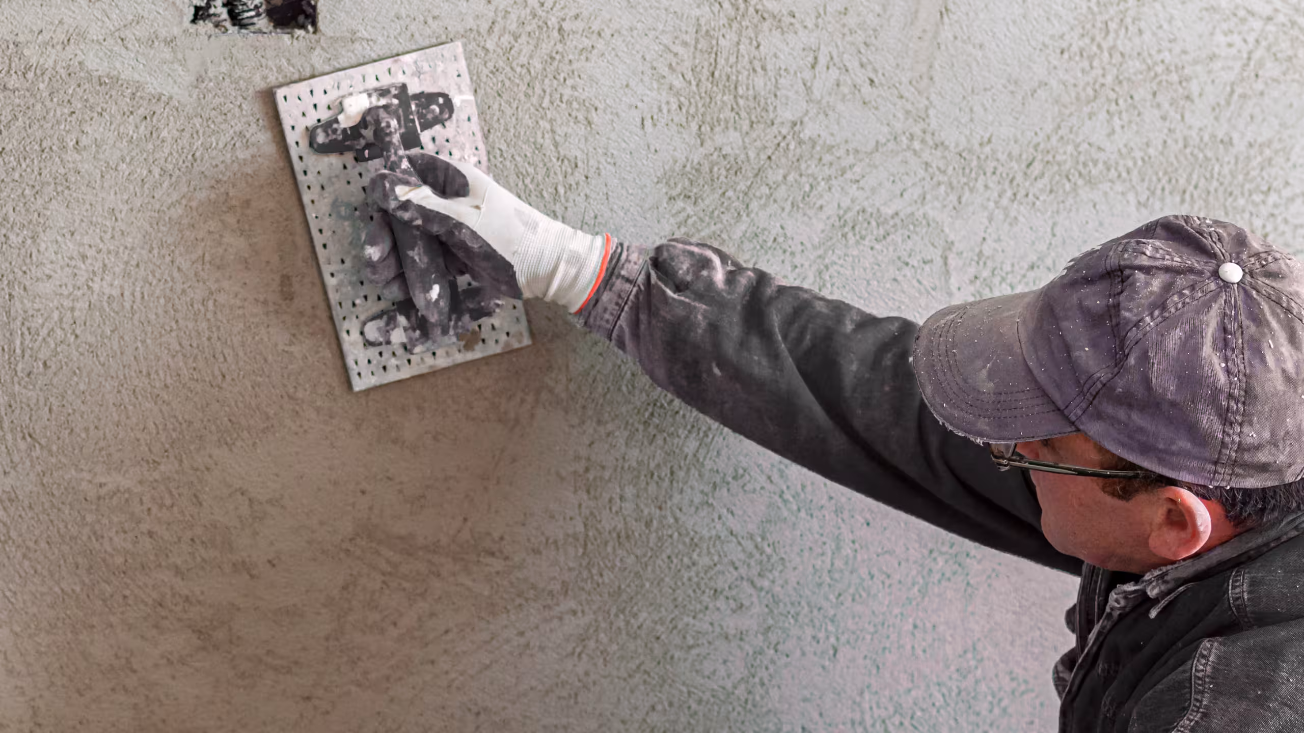 Handwerker mit Handschuhen trägt mit einer Kelle Innenputz auf eine Wand auf.