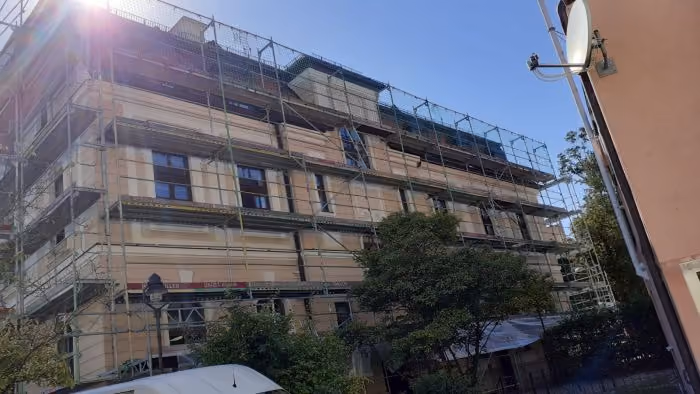 Gebäude mit Gerüst umgeben für Renovierungsarbeiten an der Außenfassade, helle Wände, mehrere Fenster, Sonnenschein und blauer Himmel im Hintergrund.