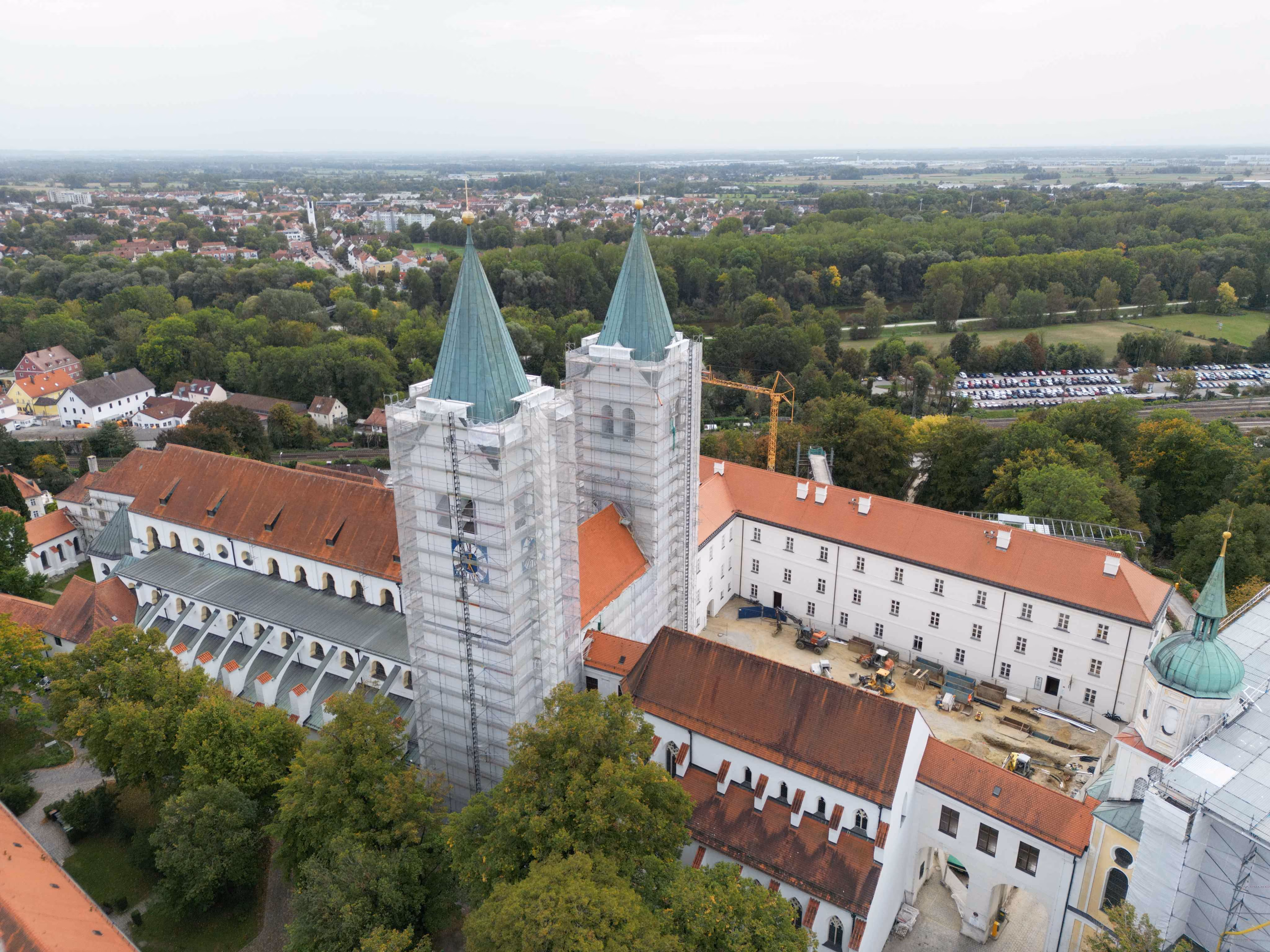 Luftbild des Freisinger Doms mit eingerüsteten Zwillingstürmen und umliegenden Gebäuden im Grünen.