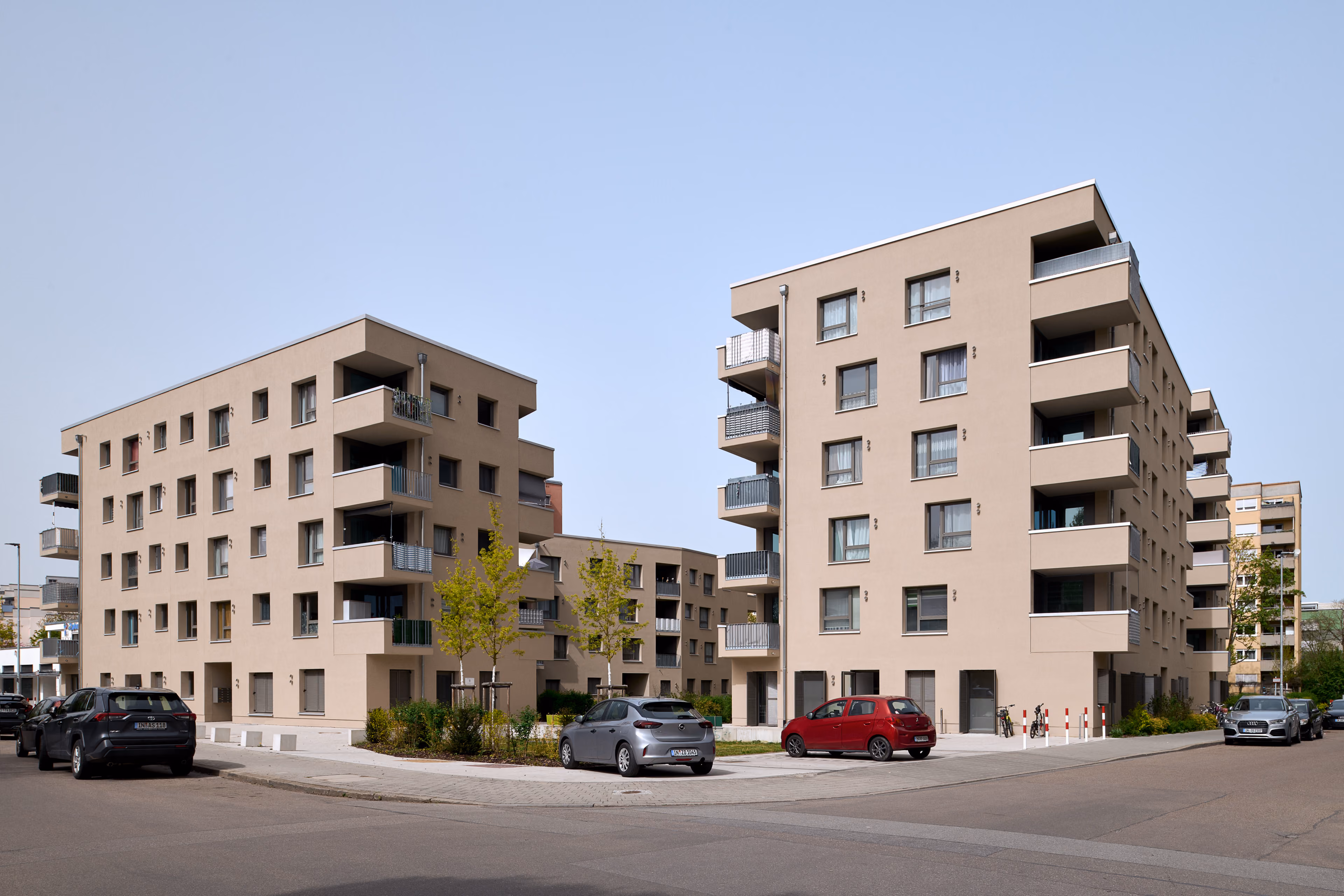Moderne Wohngebäude mit Balkonen und geparkten Autos an einer ruhigen Straßenkreuzung.