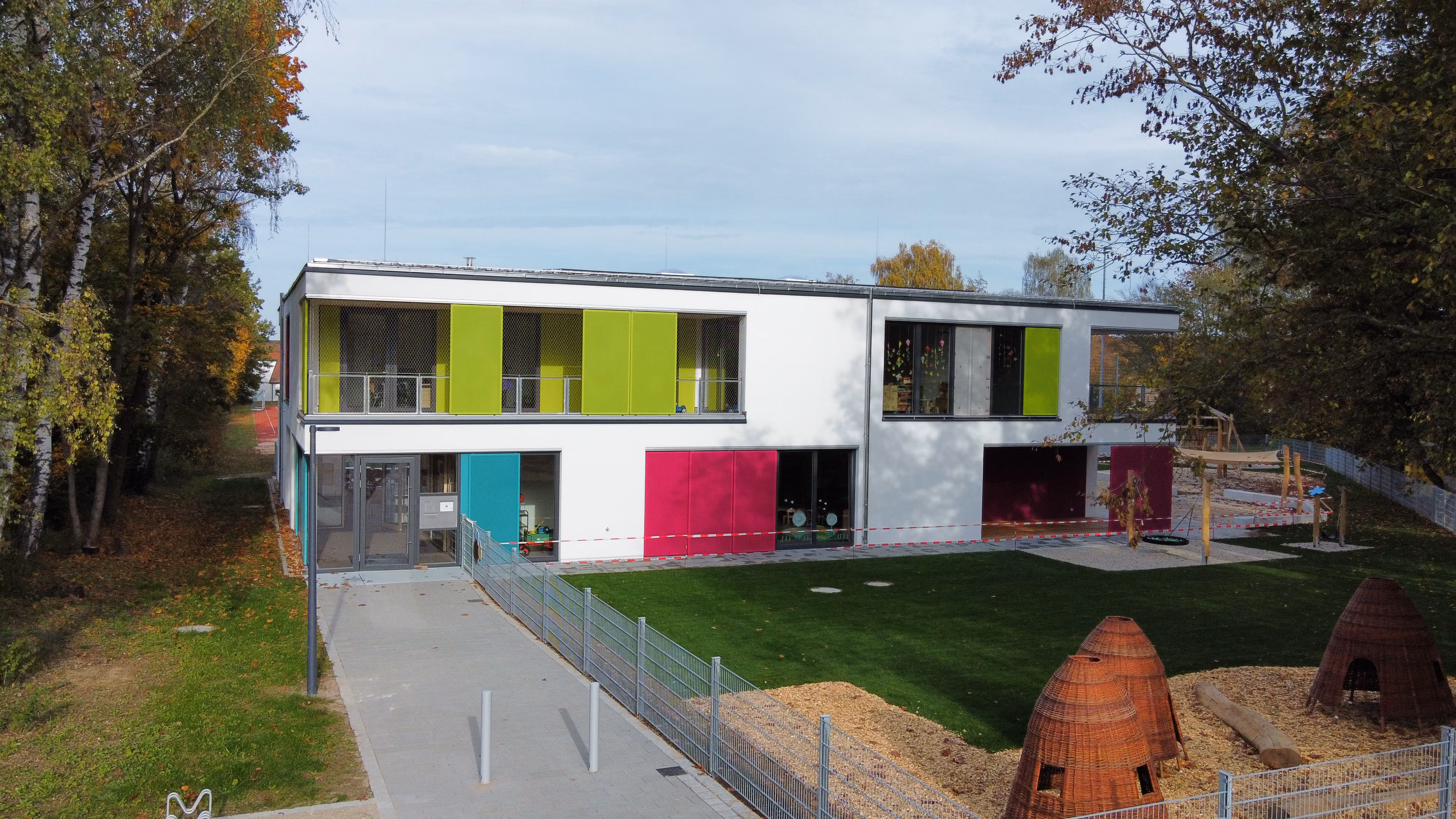 Modernes zweistöckiges Gebäude mit bunten Fensterläden und einem Spielplatz im Grünen.