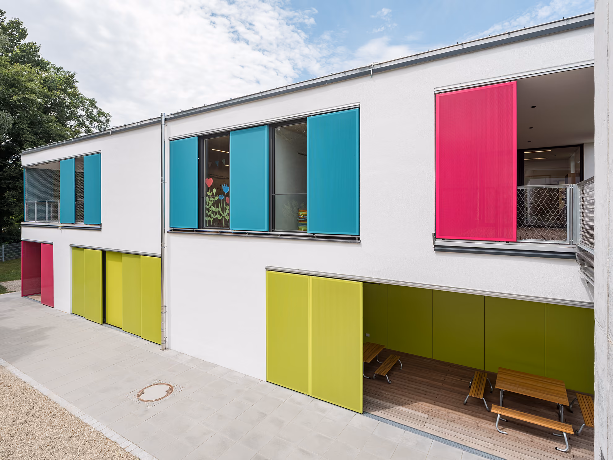 Moderne weiße Fassade mit bunten Schiebetüren in Blau, Pink und Grün an einem Gebäude.