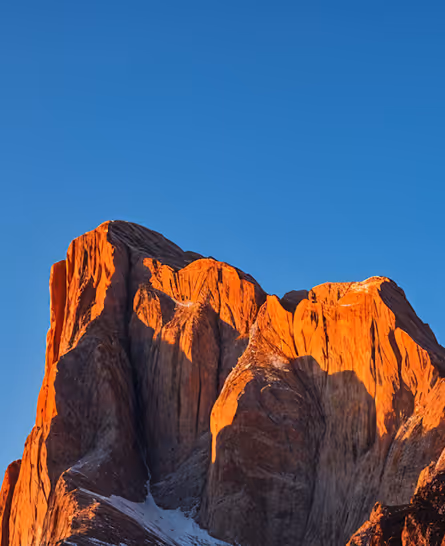 Mountain peaks bathed in bright orange sunlight against a clear blue sky.