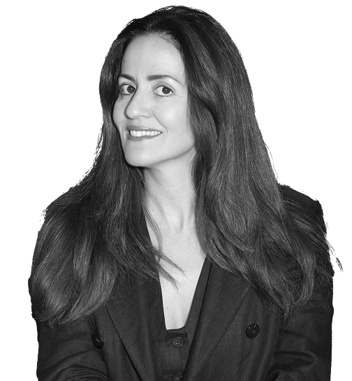 Smiling woman with long dark hair wearing a dark blazer and top on black background.