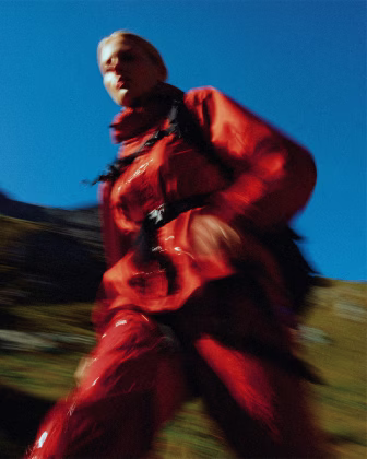 Blurred image of a person in a red jacket and pants outdoors against a clear blue sky.