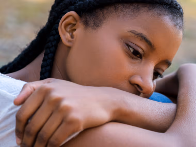Close-up of a young woman with braided hair resting her head on her folded arms, looking contemplative.