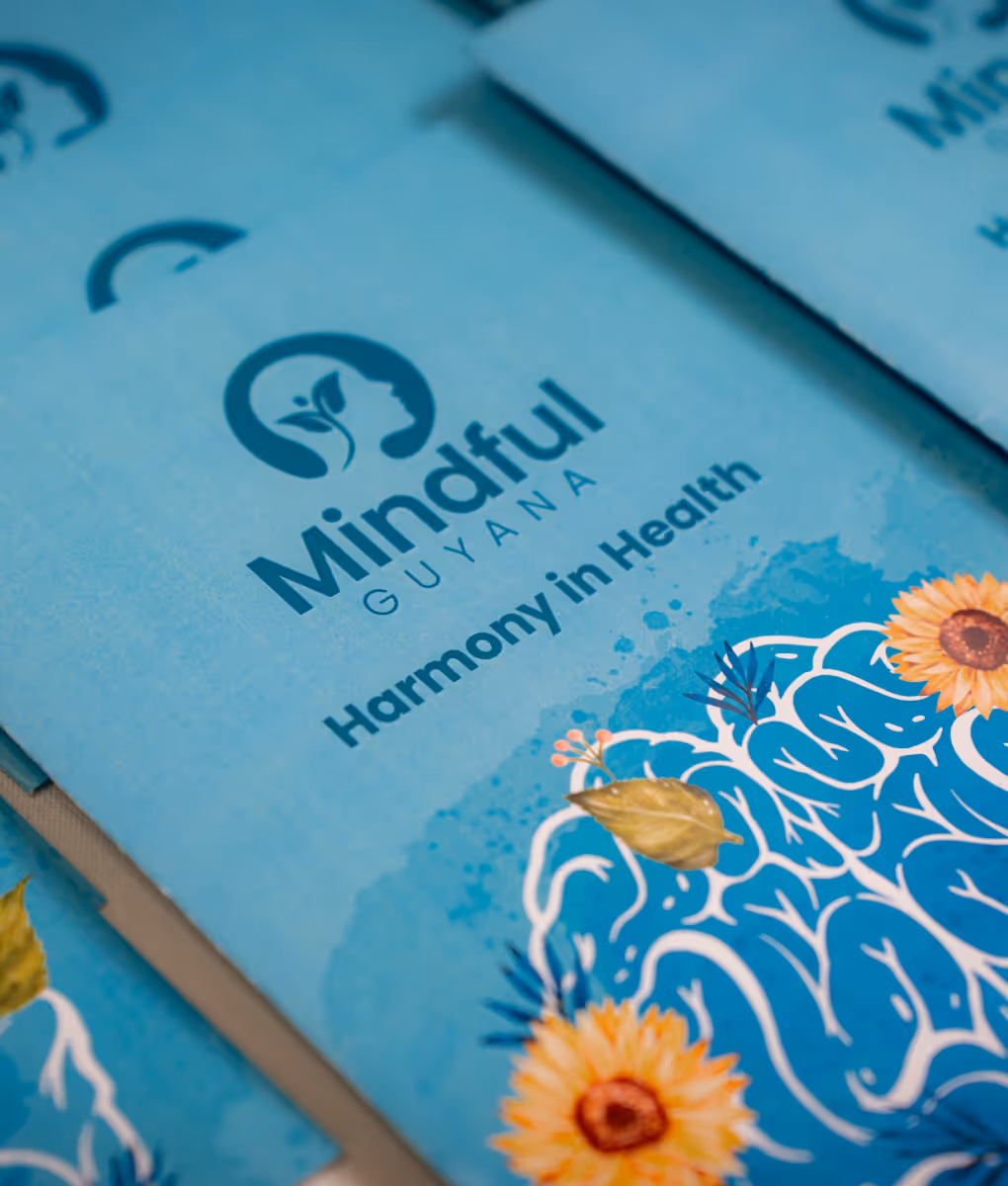 Blue brochure with logo and text 'Mindful Guyana Harmony in Health' featuring a stylized brain design with flowers and leaves.