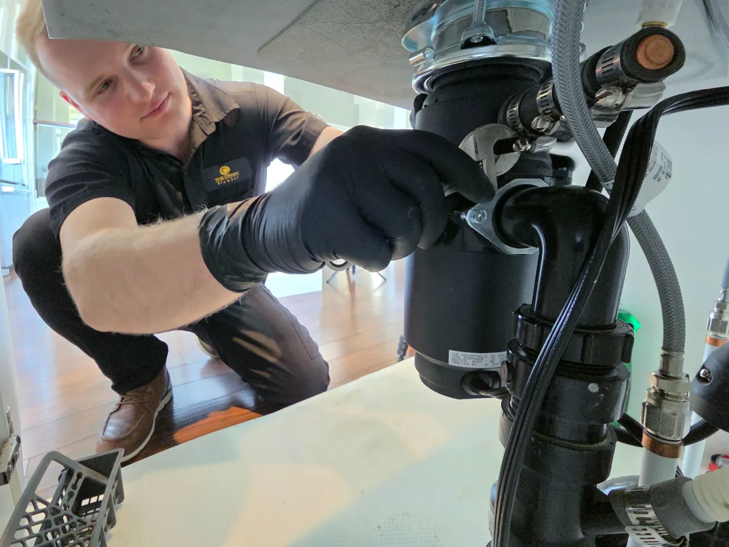 The Crazy Plumber technician Tony tightening drain fittings on a garburator installation beneath a kitchen sink in Port Coquitlam, BC