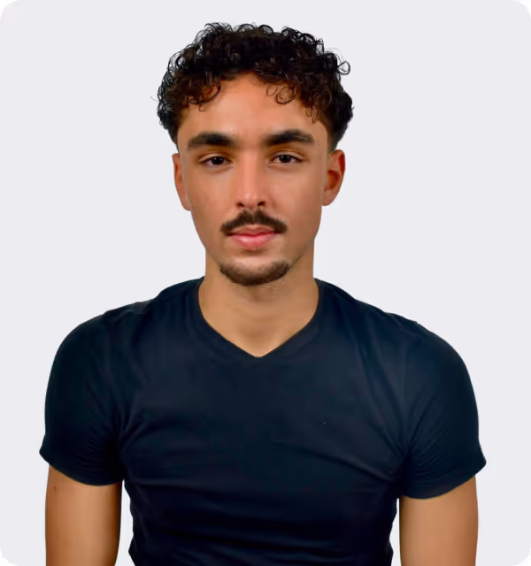 Der Webdesign Experte Faris Schmidt mit lockigem Haar und Schnurrbart, bekleidet mit einem schwarzen T-Shirt, Webflow-Experte für B2B-Webdesign.