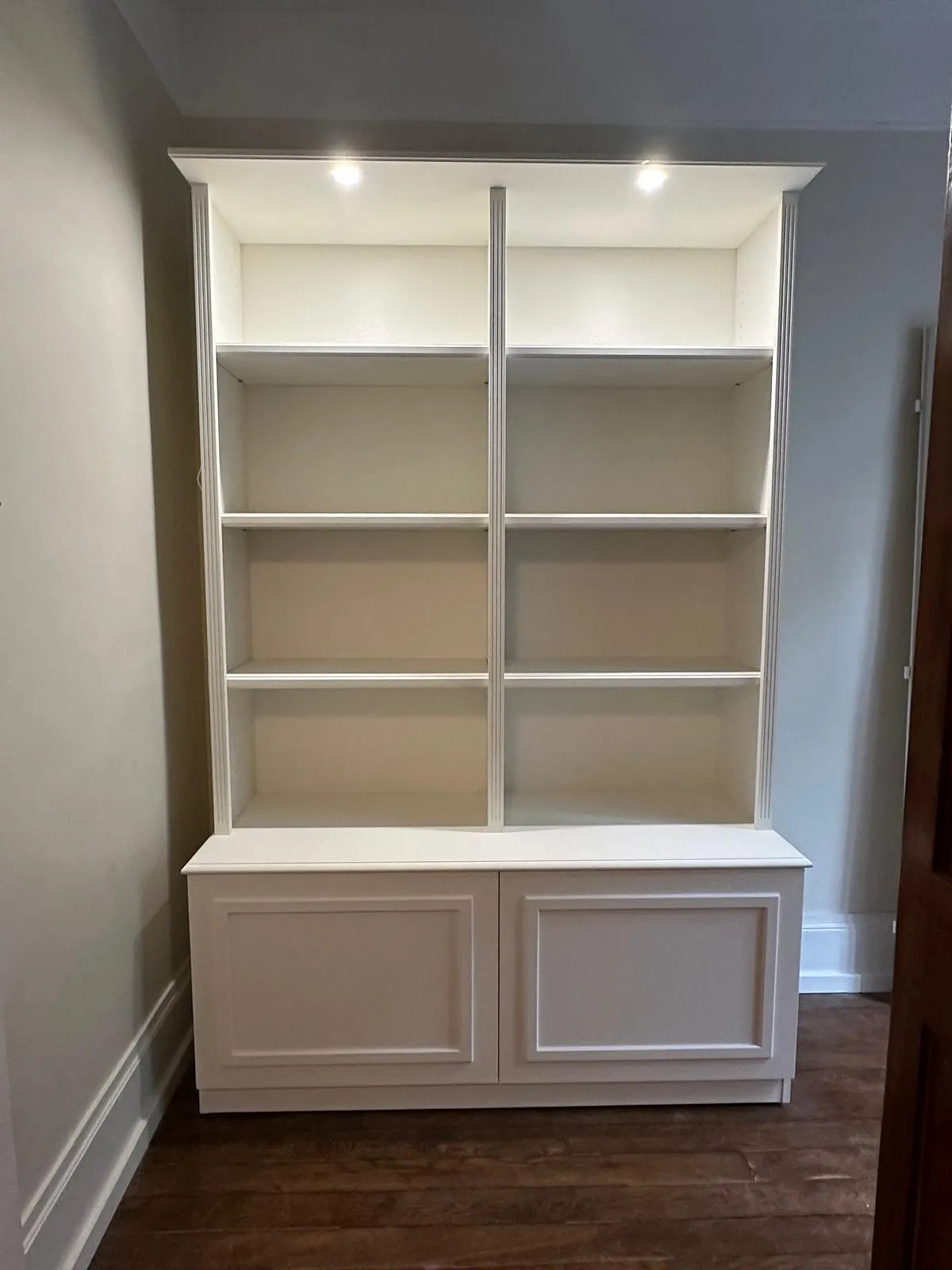 Bibliothèque blanche vide à six étagères avec deux projecteurs intégrés en haut et un rangement fermé en bas.