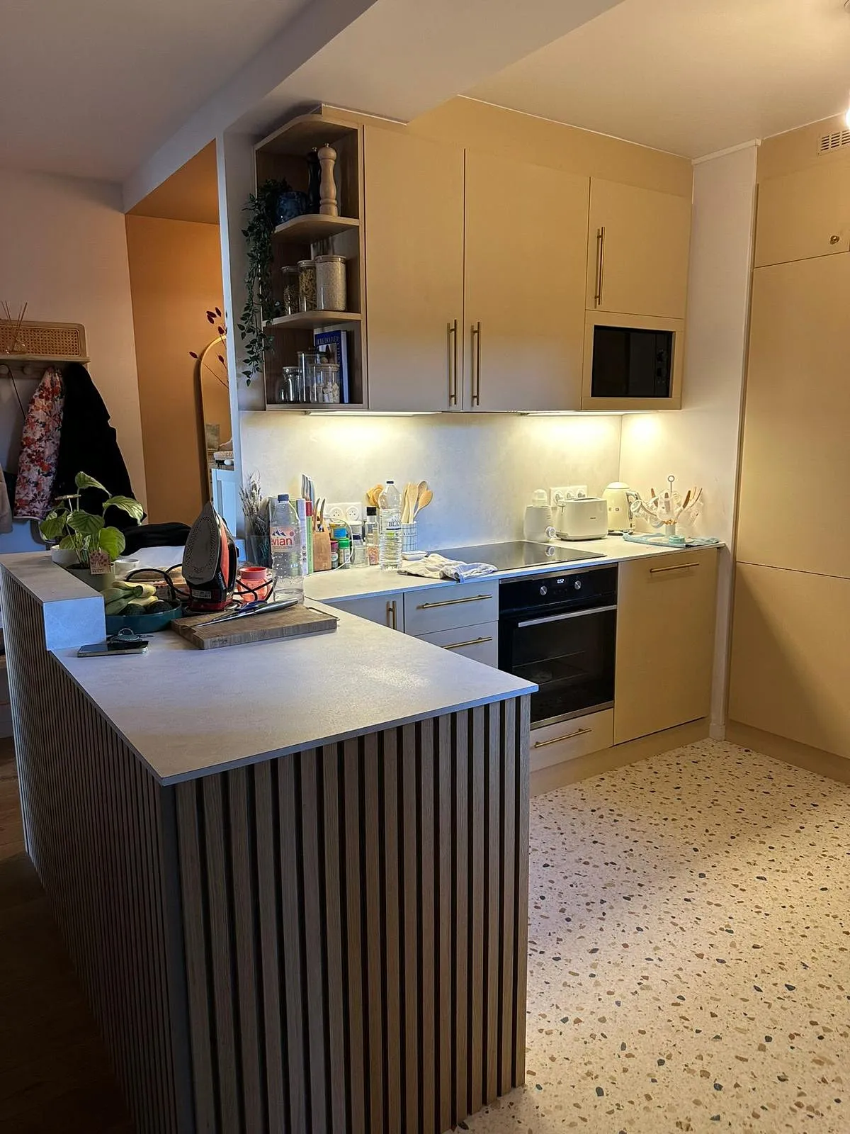 Cuisine moderne avec plan de travail clair, îlot en bois, appareils électroménagers blancs et étagères ouvertes avec bocaux.