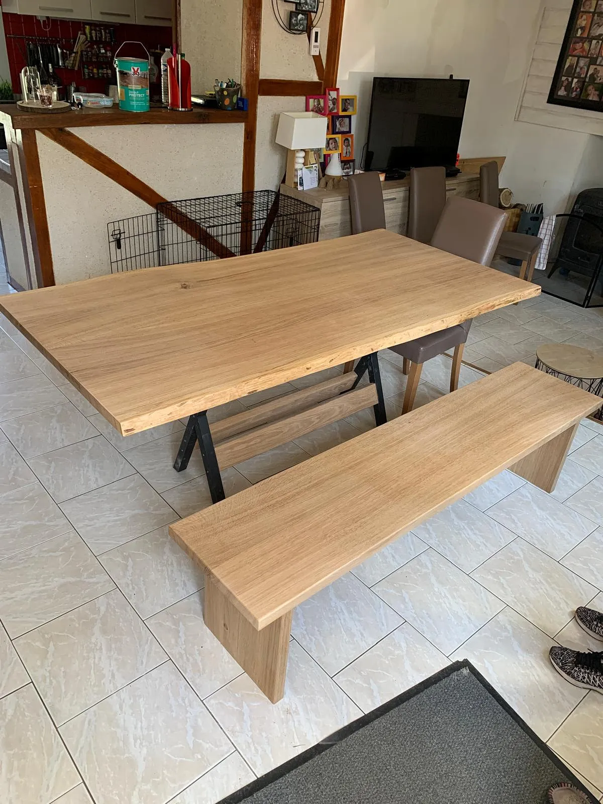Table en bois clair avec un banc assorti et quatre chaises en cuir marron dans une salle à manger carrelée.