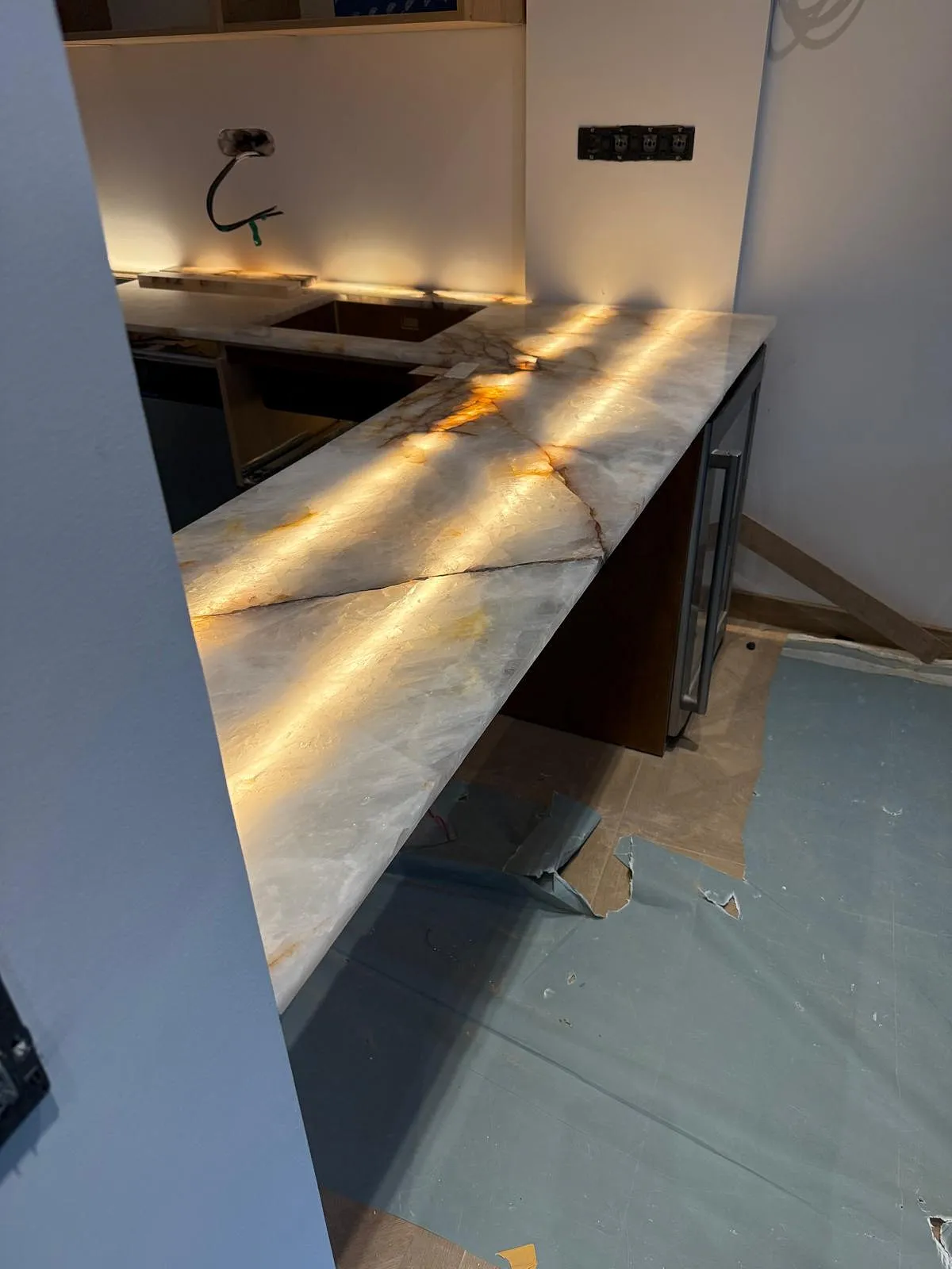 Plan de travail en marbre avec des veines brunes, éclairé par une lumière chaude, en cours d'installation dans une cuisine.