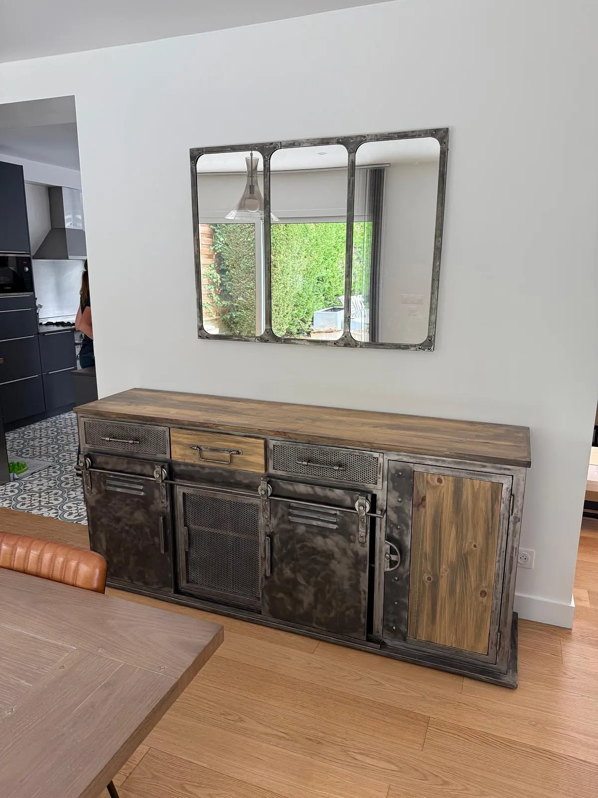 Buffet industriel en bois et métal avec miroir triple au-dessus, dans une pièce à sol en bois clair.