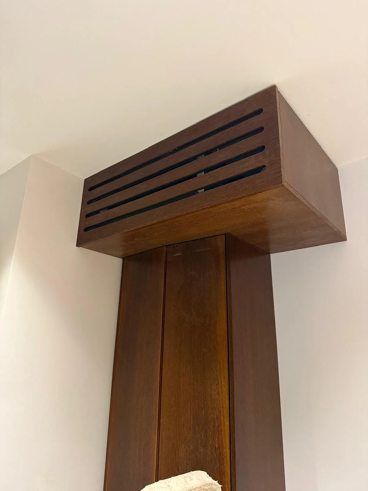 Élément en bois foncé fixé au plafond, avec des fentes horizontales sur le côté supérieur.