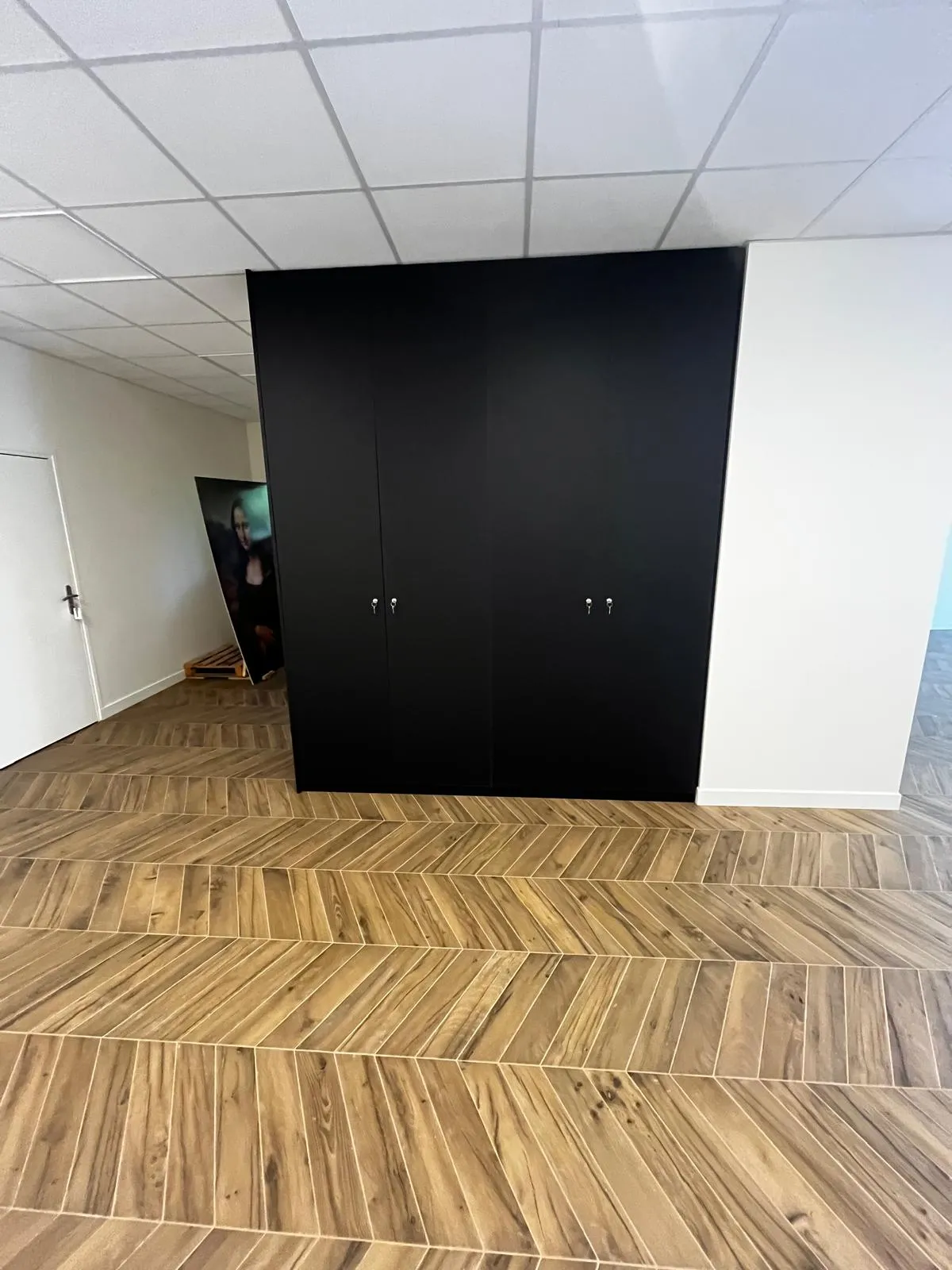 Grand placard noir avec quatre portes et clés dans une pièce avec un sol en bois clair en chevrons et un plafond blanc à dalles.