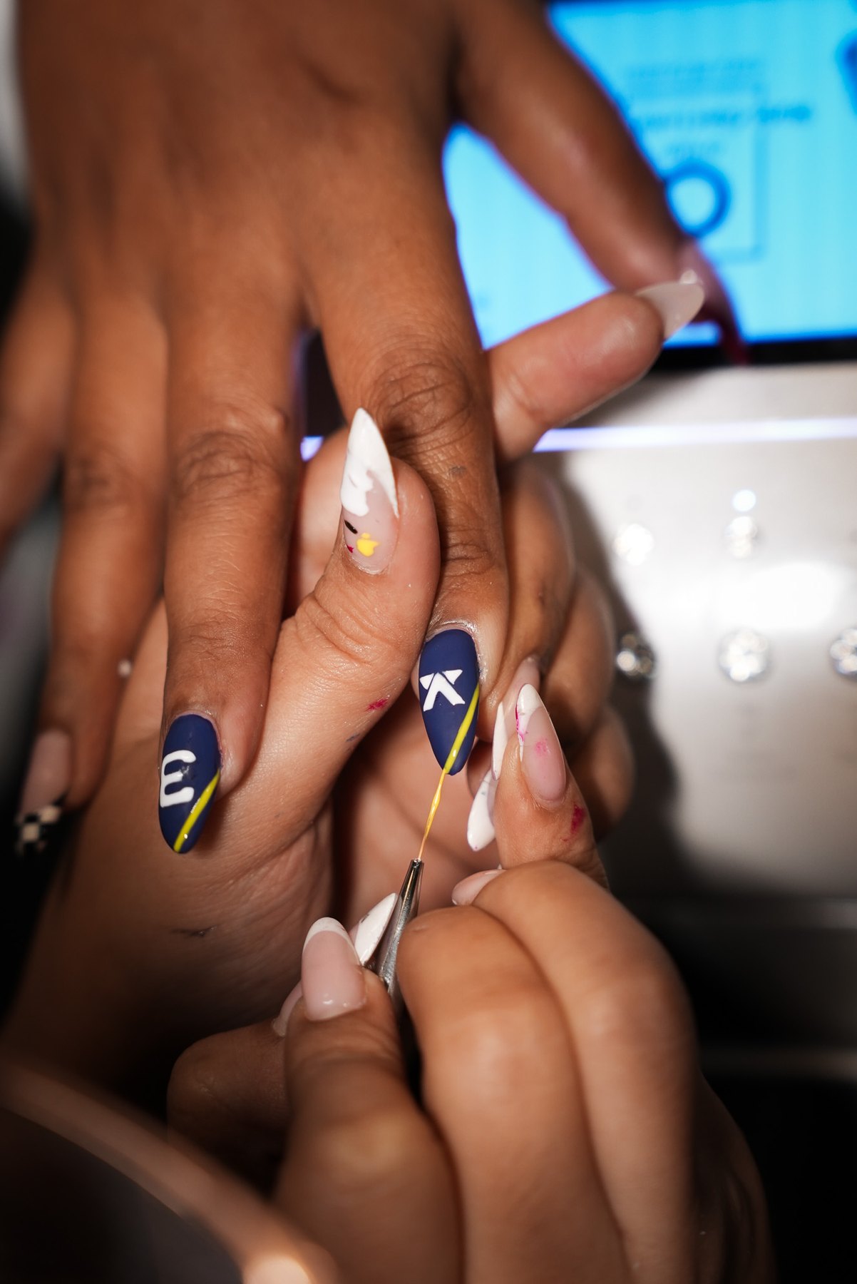 Nail artist drawing a yellow racing pinstripe with a liner brush on navy F1 nail art in Dubai