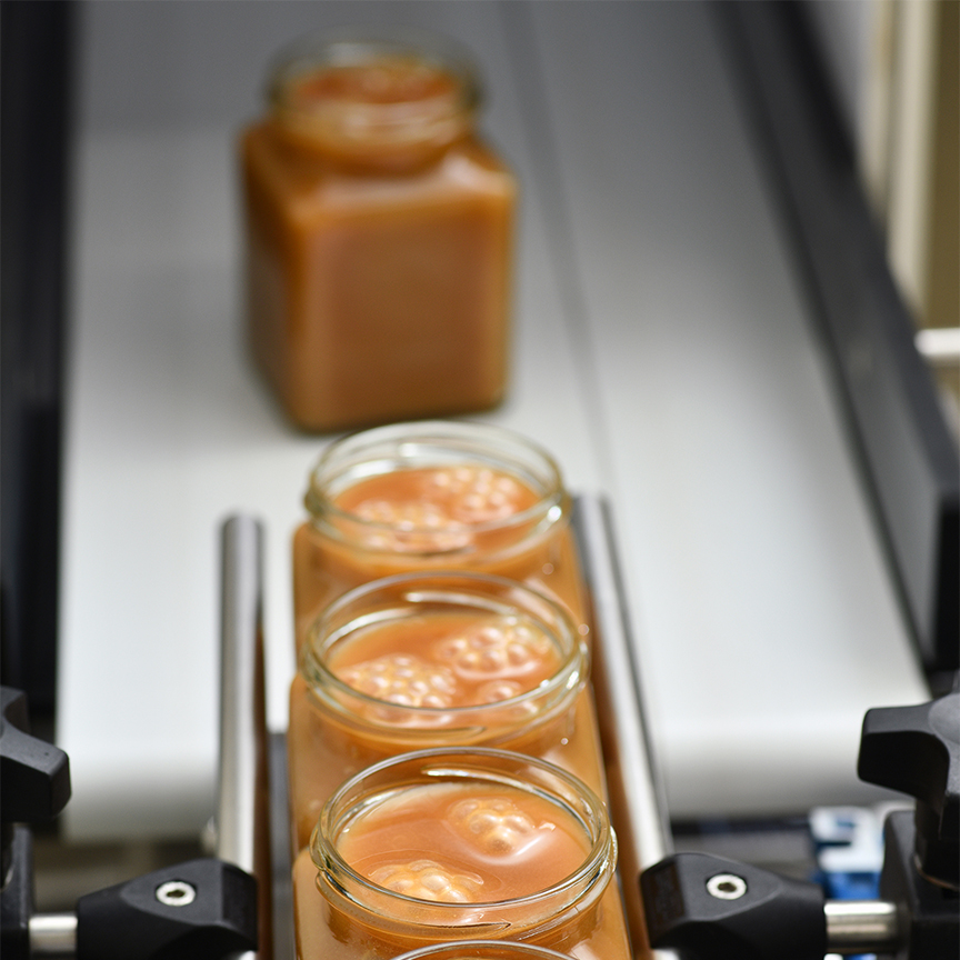 Glass jars filled with orange liquid and bubbles on a conveyor belt.