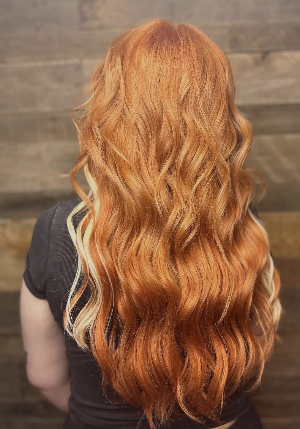 Back view of a person with long, wavy vibrant orange hair with a few light blonde streaks.