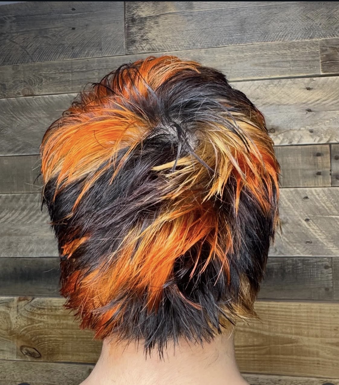 Short, layered hairstyle dyed in bright orange, black, and blonde colors.