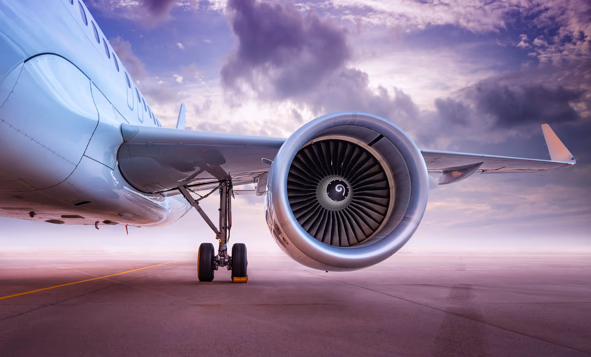 Close-up of airplane engine and landing gear on runway with cloudy sky backdrop.