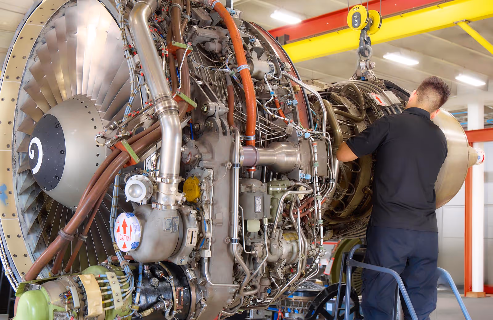 Technician wearing black shirt inspecting a large aircraft jet engine in a maintenance shop in Advanced Turbine Systems.