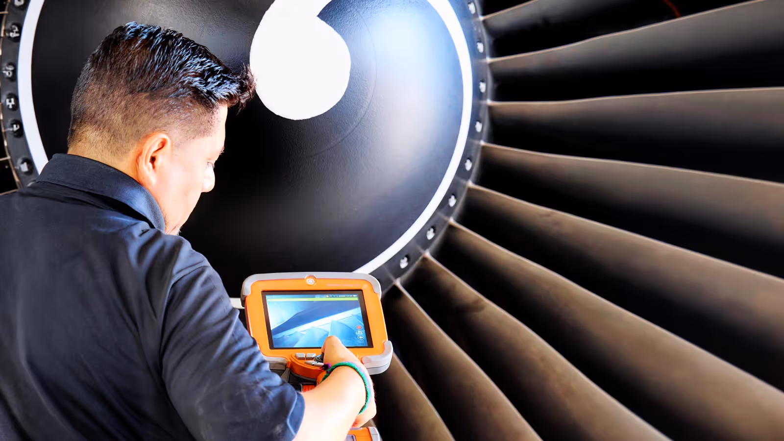 Technician from Advanced Turbine Systems inspecting large turbine blades using a handheld device with a screen showing blade details.