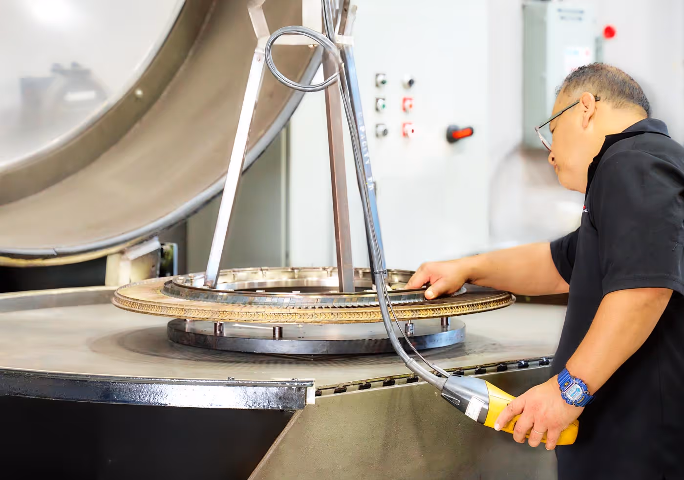 Technician from Advanced Turbine Systems inspecting a large metallic turbine component with a handheld diagnostic tool.