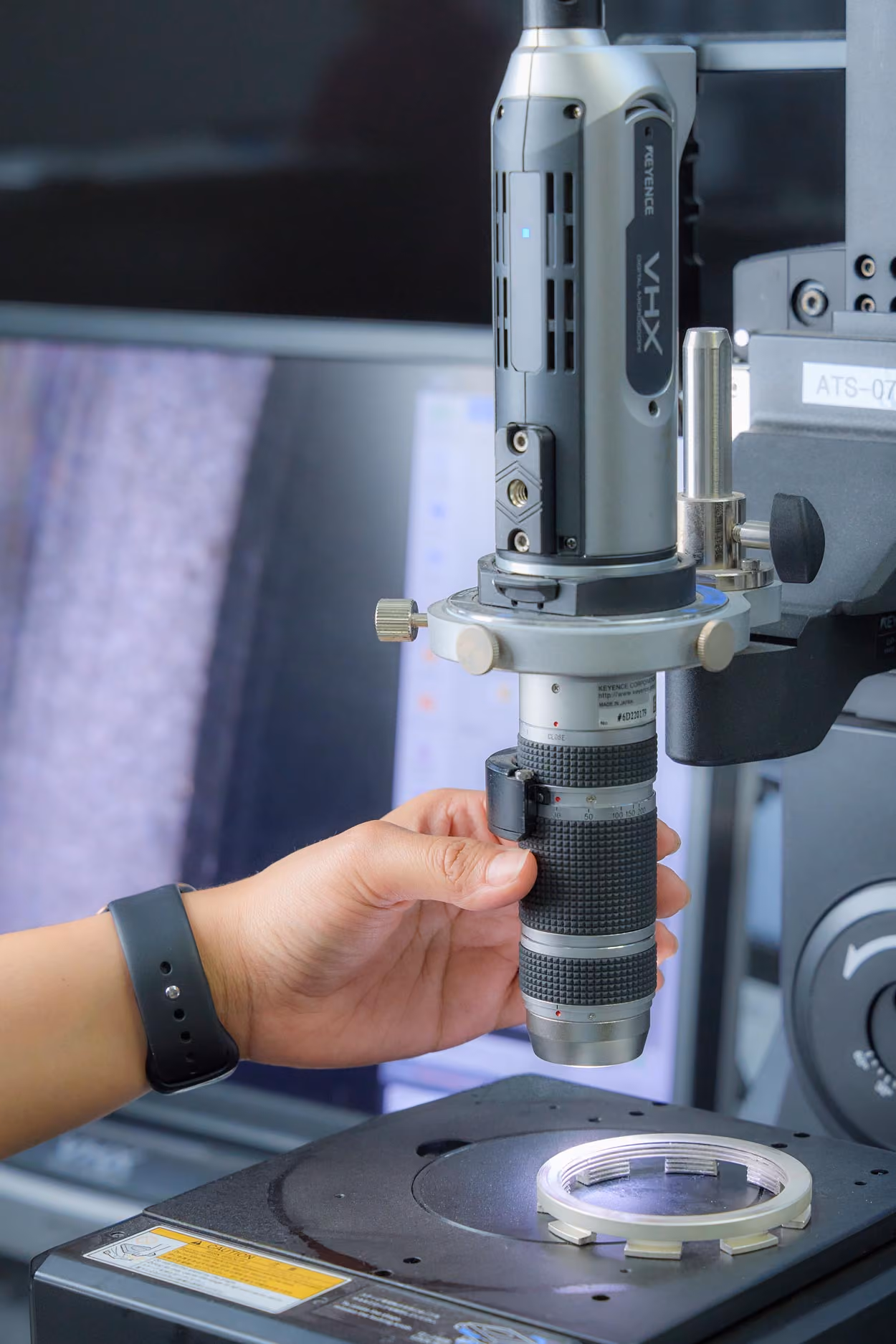 Hand of a technician from Advanced Turbine Systems adjusting a Keyence VHX microscope lens over a metallic ring on the platform.