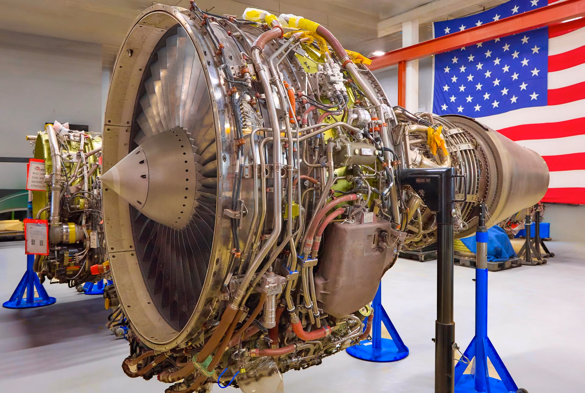 Large aircraft jet engine on stands inside a shop of Advanced Turbine Systems LLC with a U.S. flag in the background.