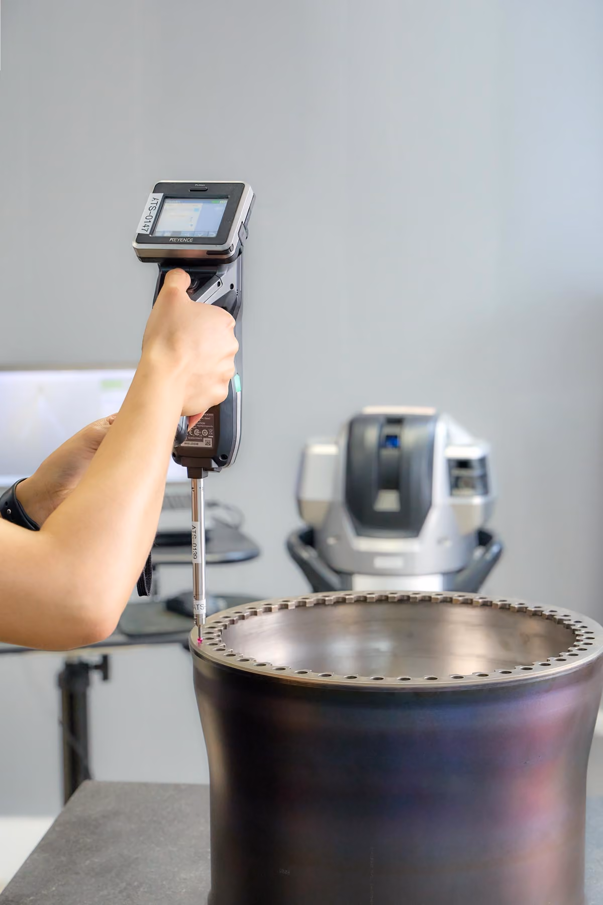 A technician form Advanced Turbine Systems, LLC uses a handheld measuring device to inspect a large metal component with multiple holes.