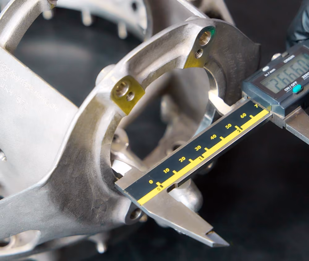 Digital caliper measuring the inner diameter of a aircraft engine metal mechanical part against a black background.