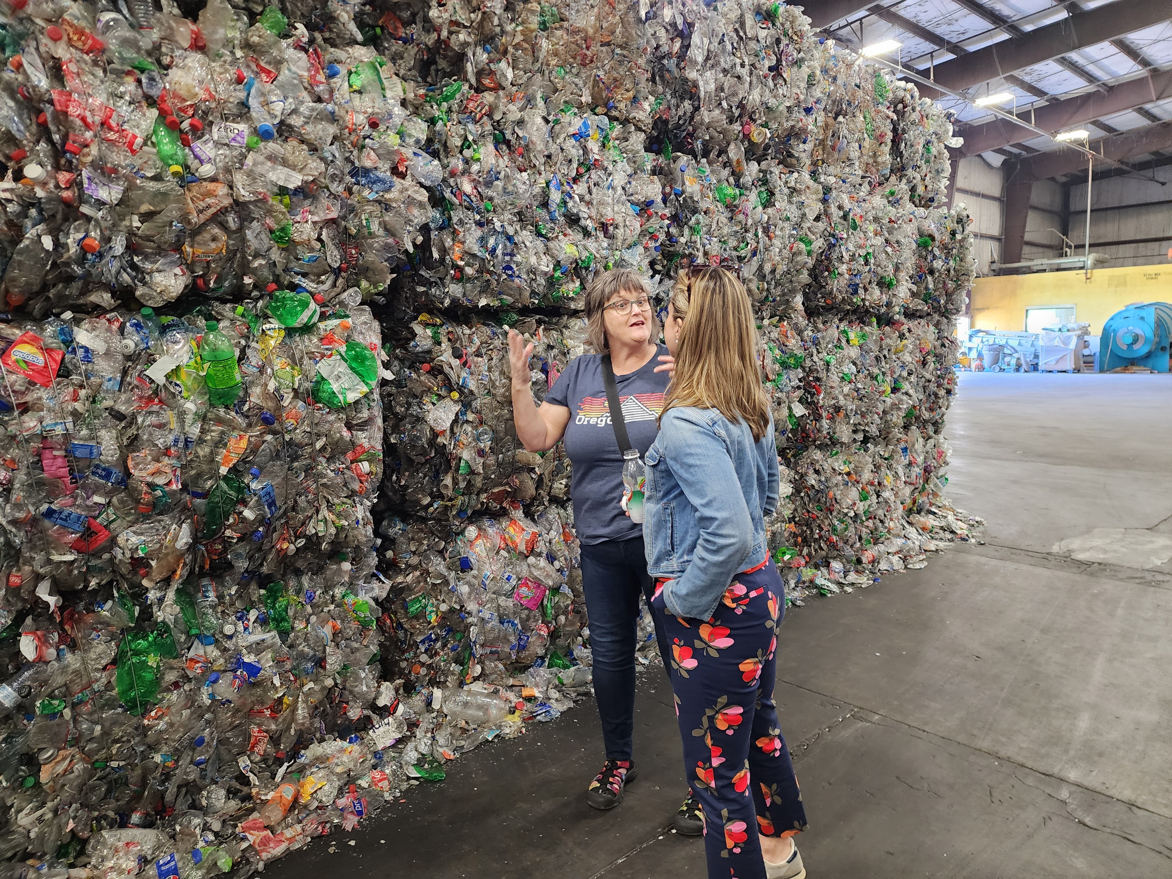 Two Circle members in conversation beside a wall of baled plastic at an Oregon recycling facility.
