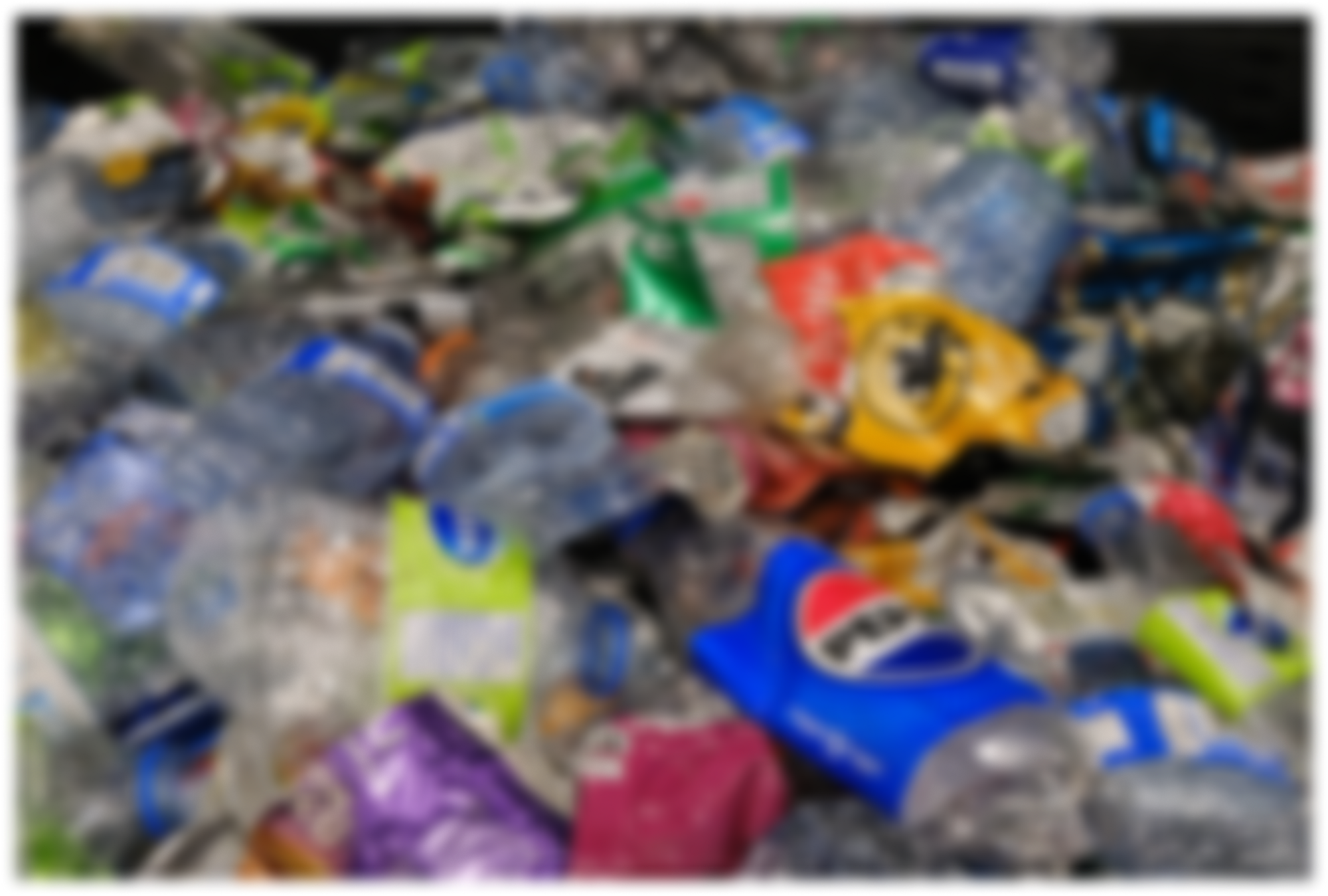 A heap of crushed plastic bottles and containers, including a blue bottle with a red and white label, mixed with various colorful packaging waste.