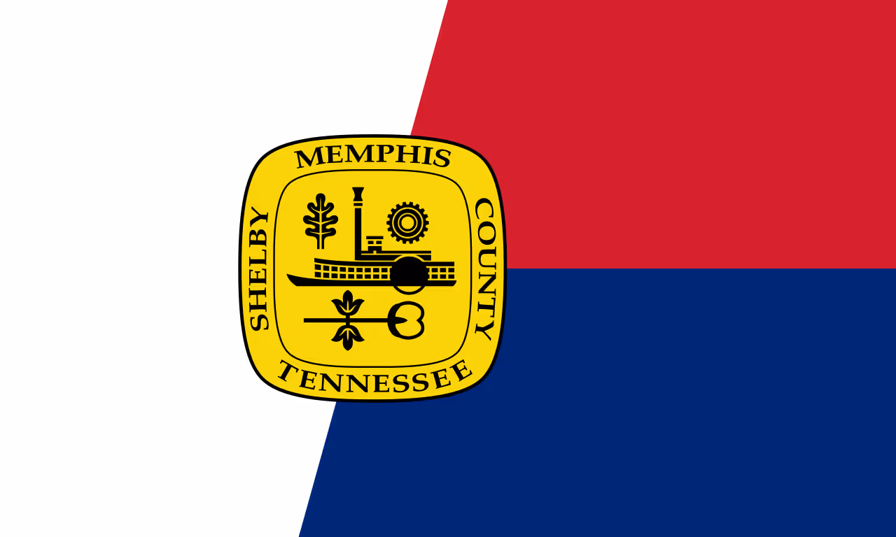 Flag of Shelby County, Tennessee, divided into white, red, and blue sections with a yellow badge featuring a riverboat and industrial symbols.