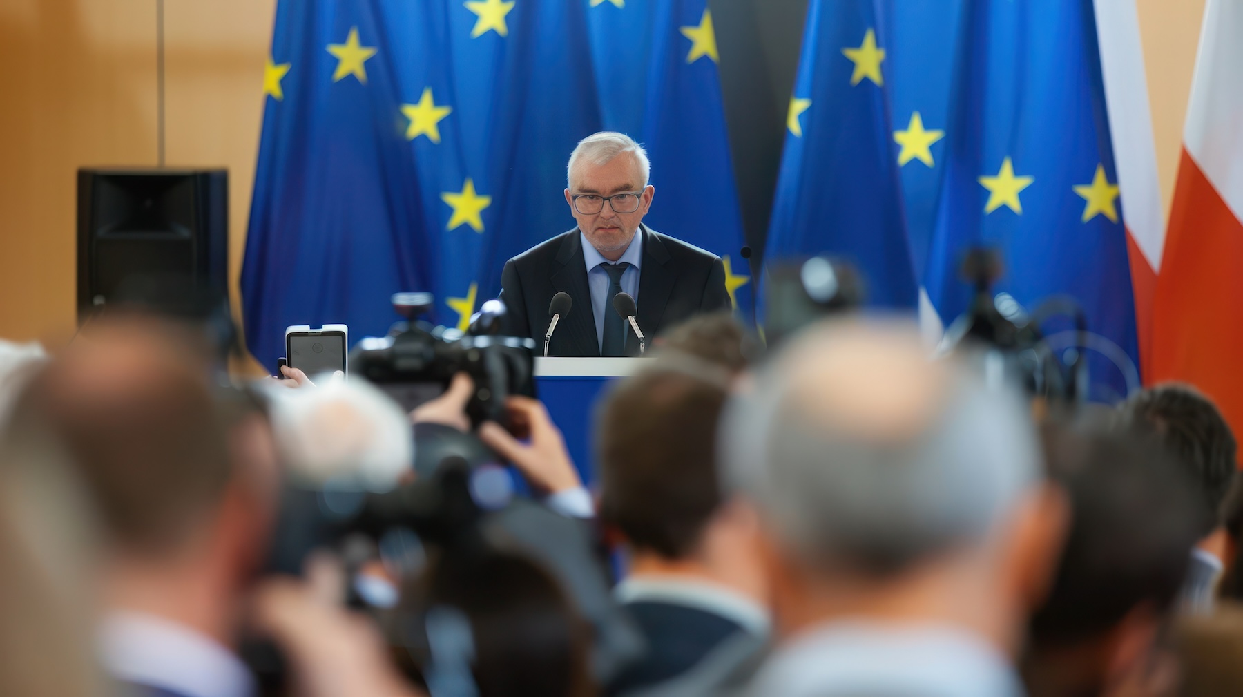 Un dirigeant en conférence de Presse face à des micros et derrière des drapeux