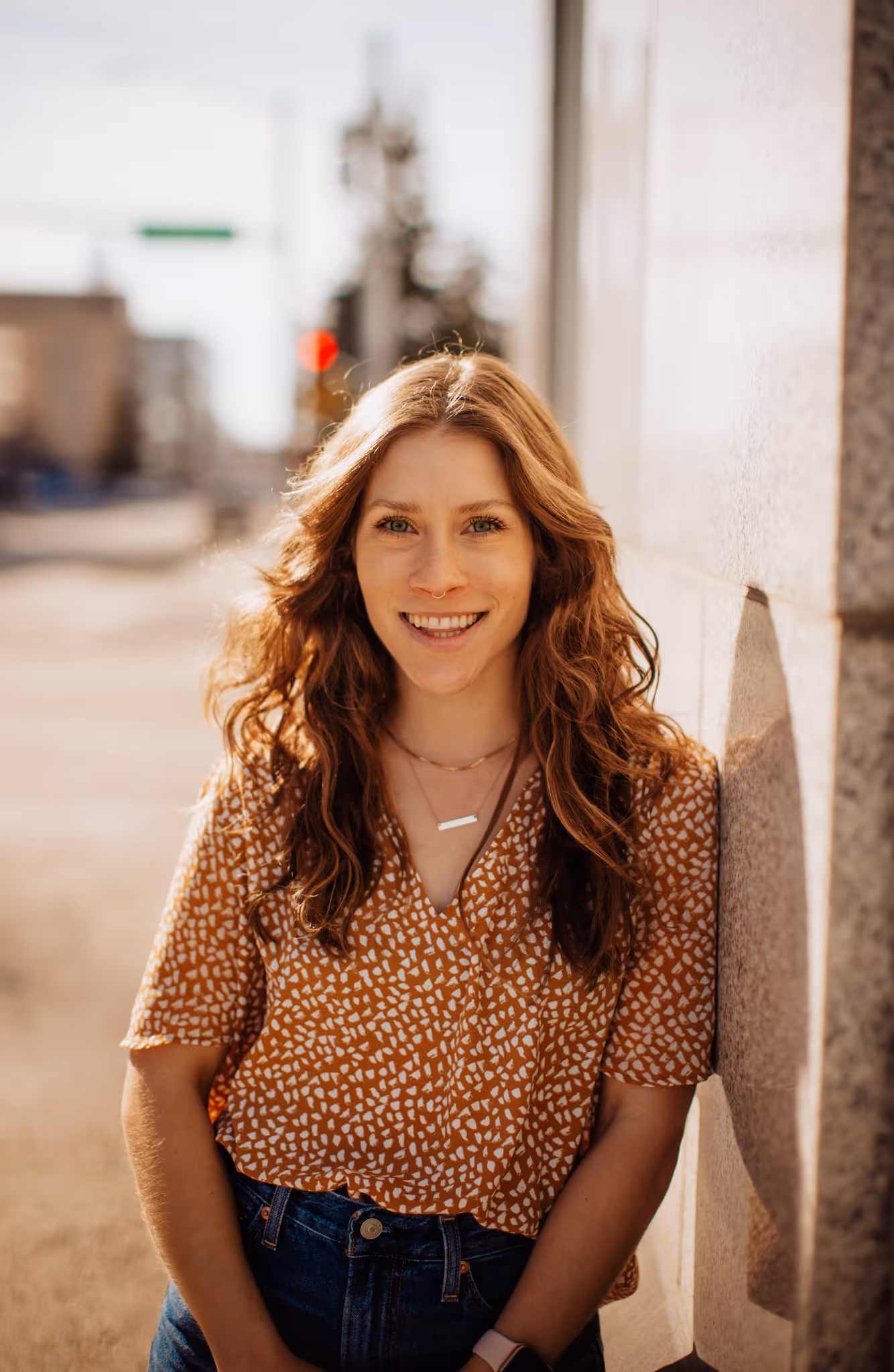Moriah smiling, leaning against a wall in a yellow shirt.