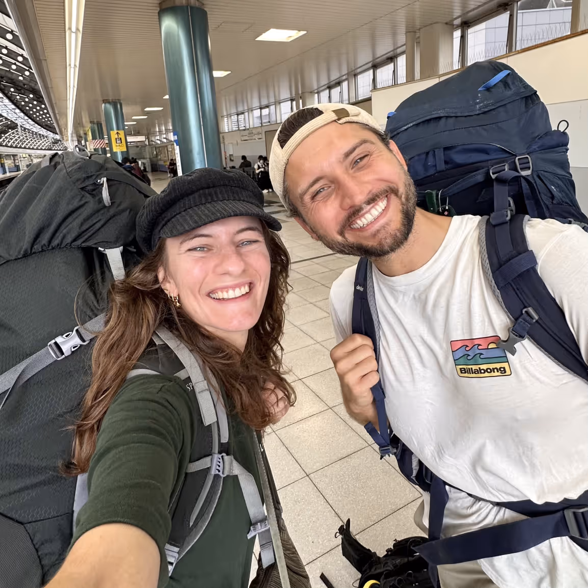Image of Sascha and Sandra, Selfie, Smiling, with backpacks at the train station