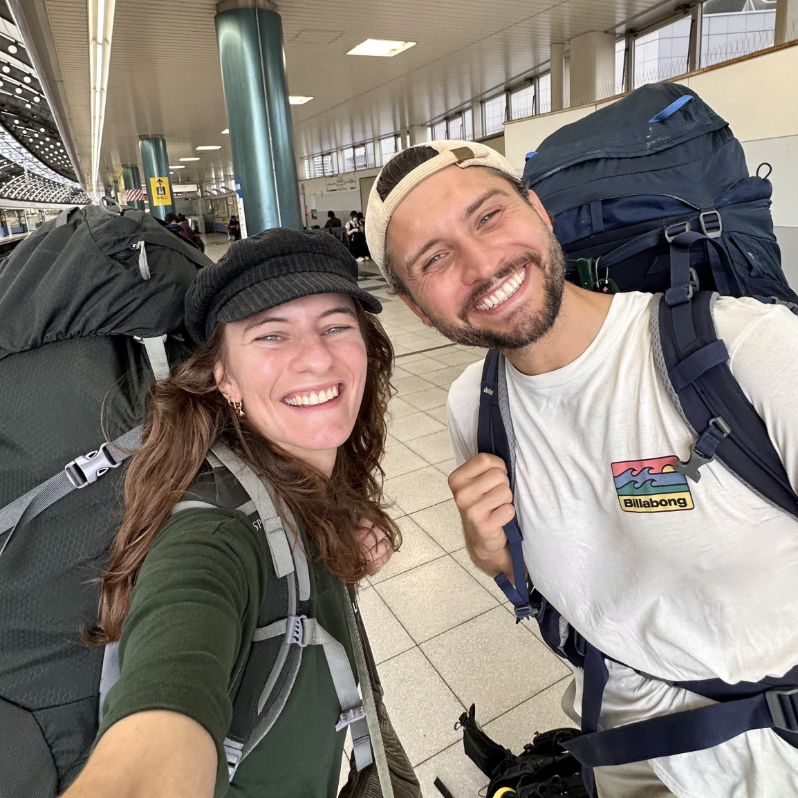 Image of Sascha and Sandra, Selfie, Smiling, with backpacks at the train station
