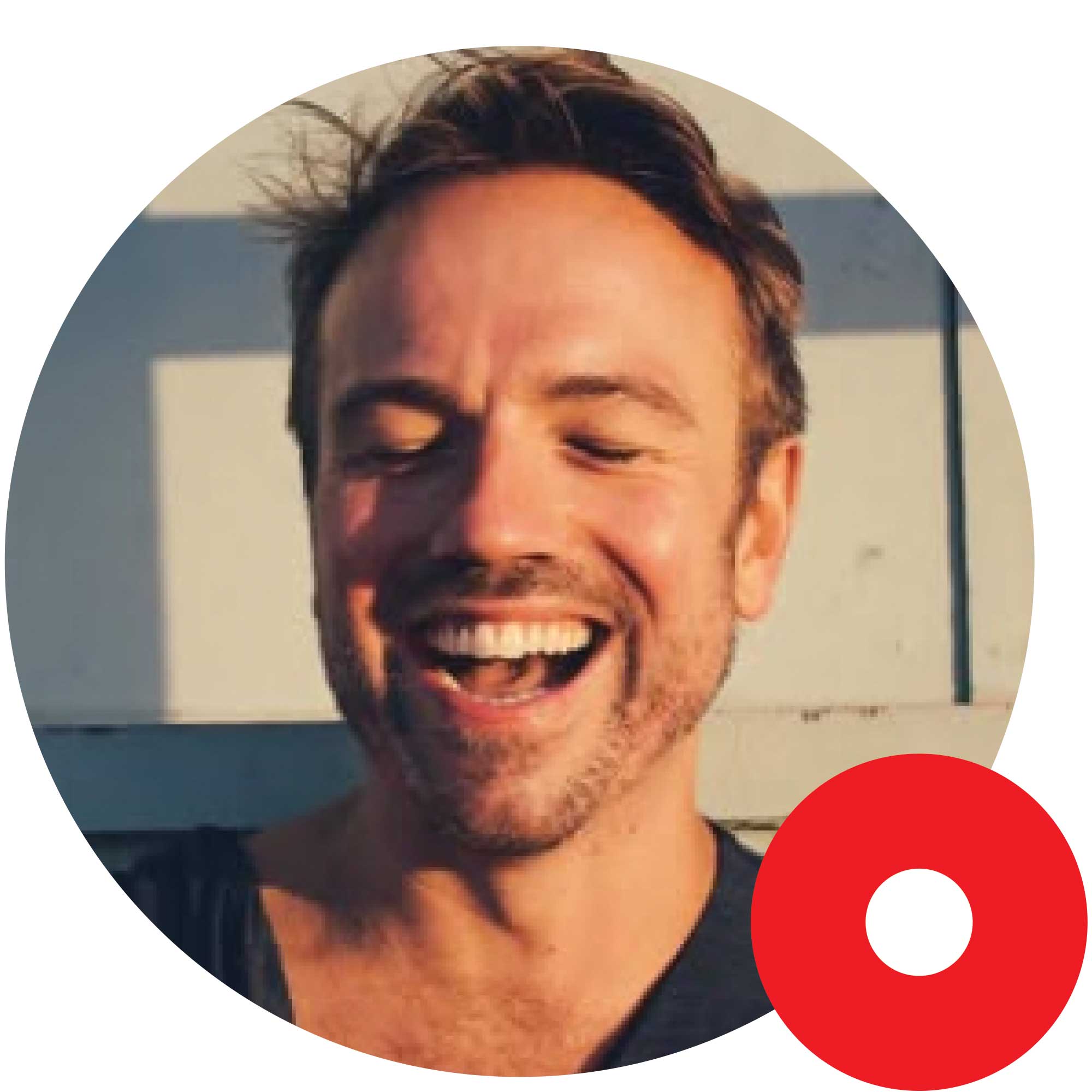 Smiling man with closed eyes and tousled hair lit by warm sunlight, wearing a dark shirt.