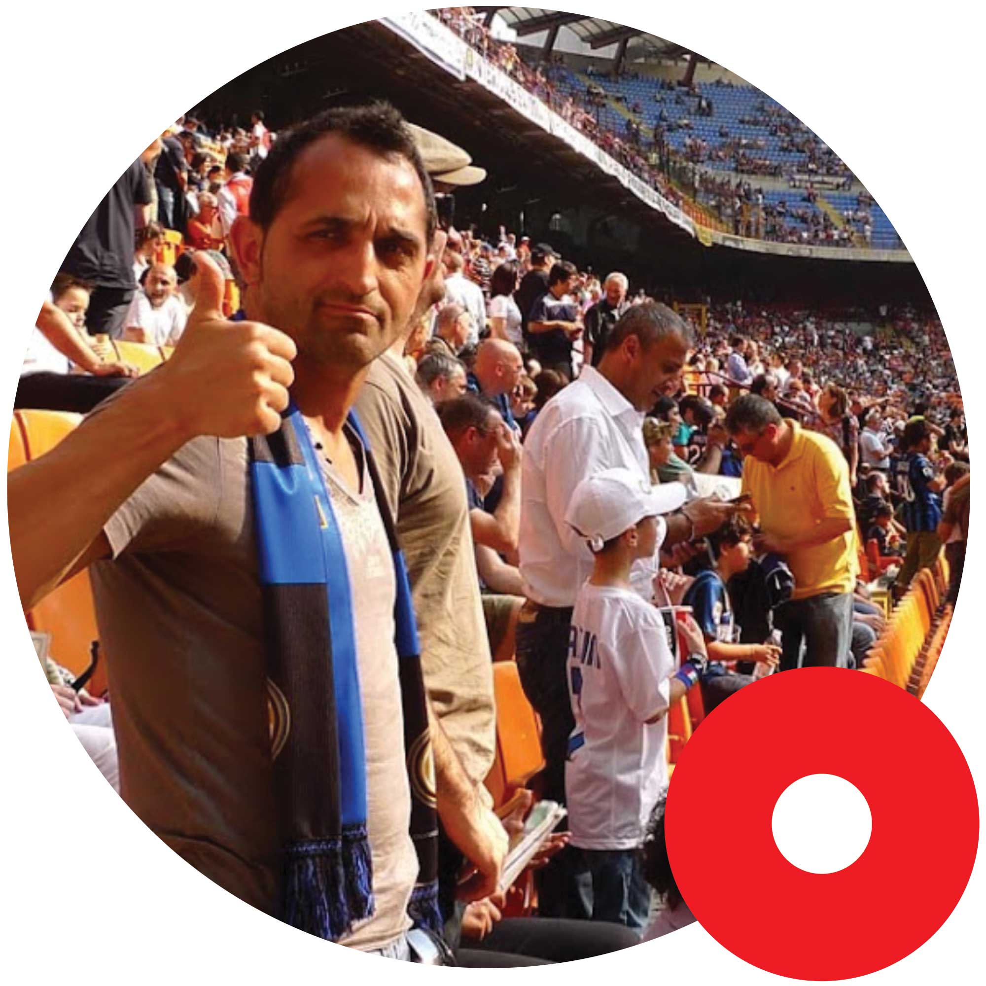 Man at a crowded sports stadium giving a thumbs-up, wearing a brown shirt and blue-and-black scarf.